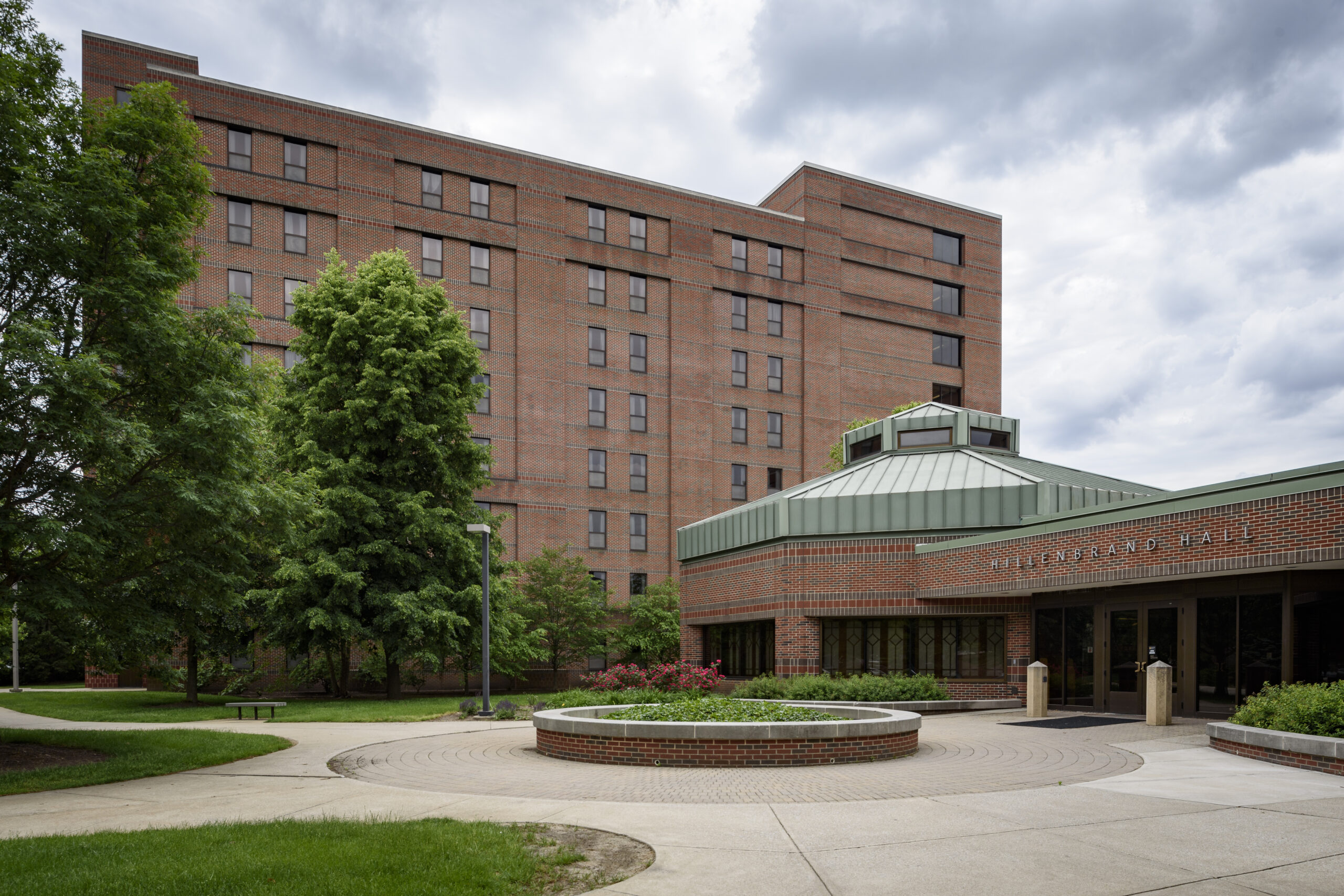 Hillenbrand Hall, tall brick residence hall with copper green dome, with trees in front