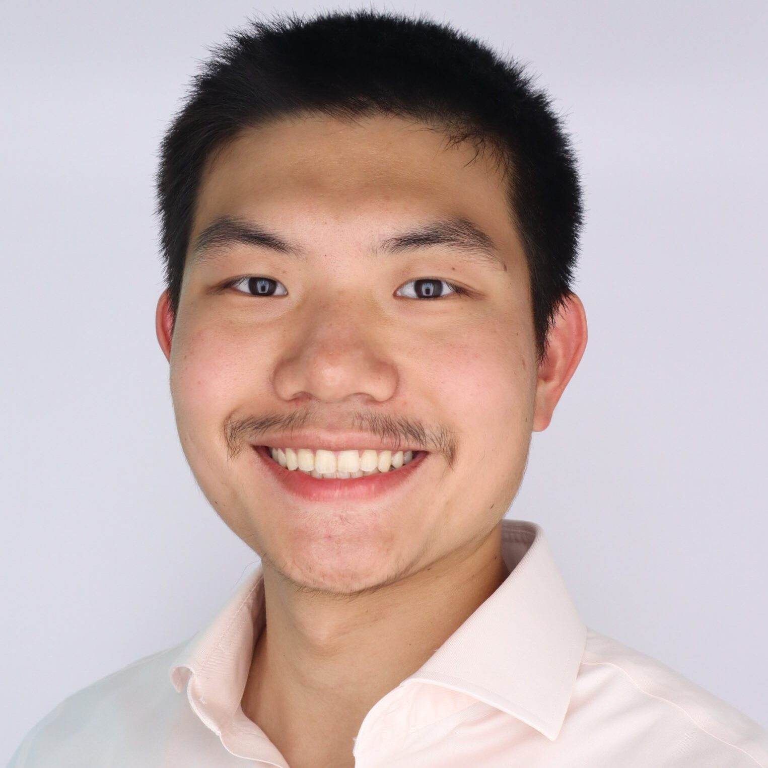 Headshot of a young man with short black hair. He is wearing a light peach button-up.