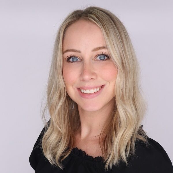 Headshot of a smiling woman with blonde hair and blue eyes, wearing a black blouse.