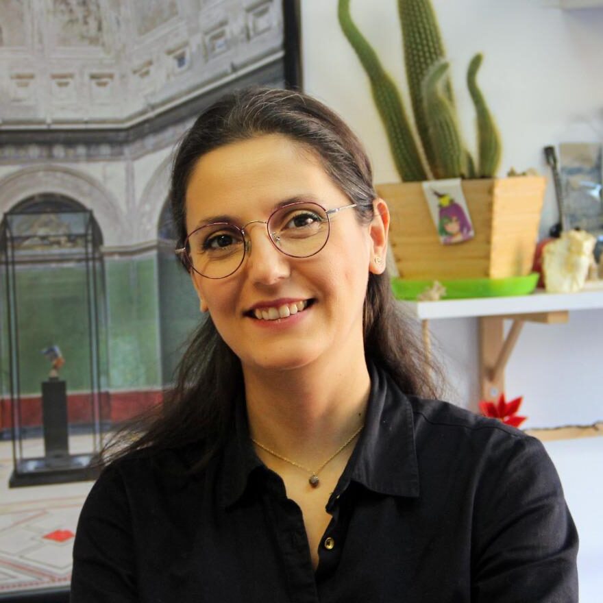 Woman with long dark hair, wearing round glasses and a black top.