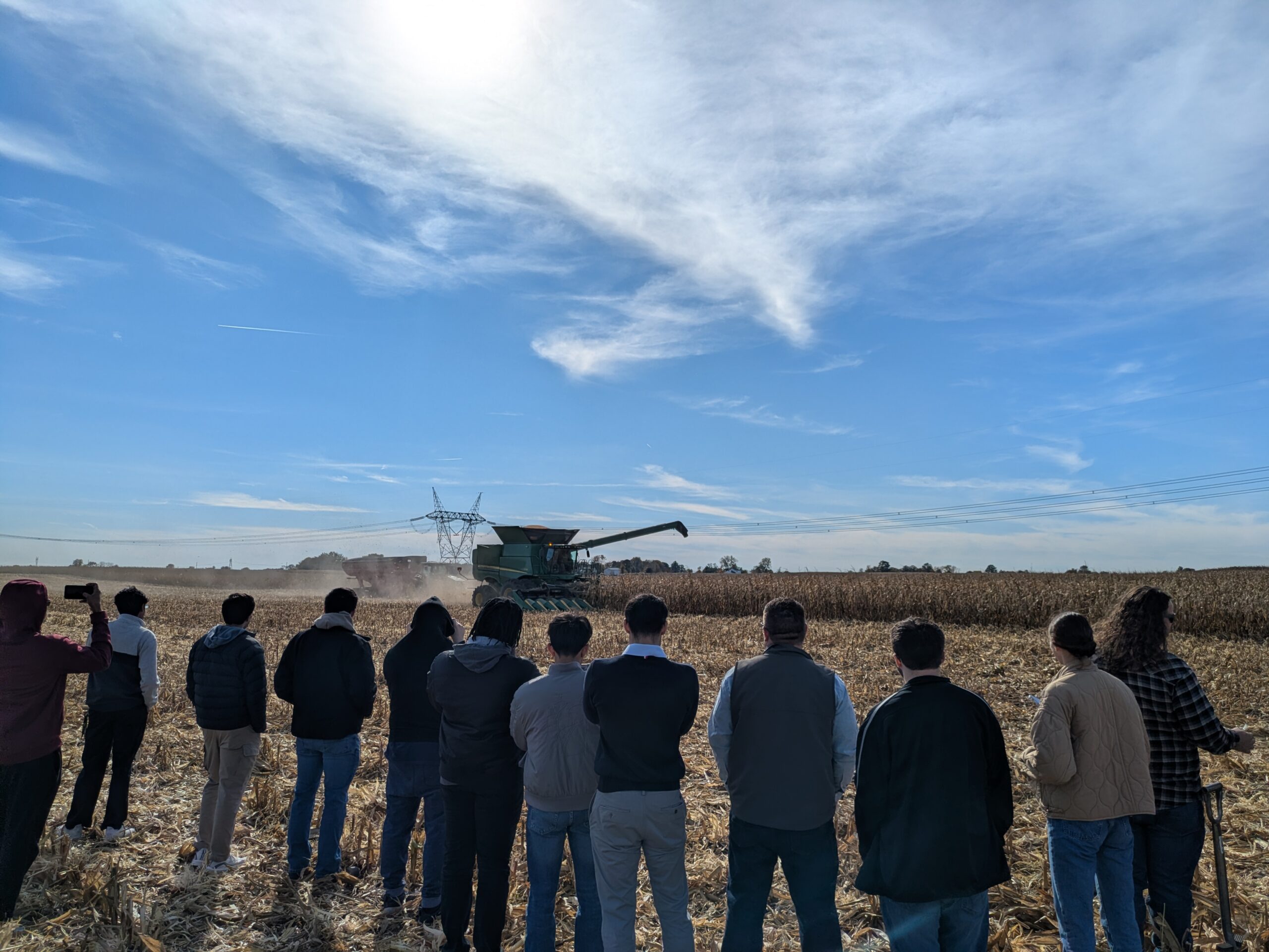 Students are facing away and looking at a harvesting corn combine.