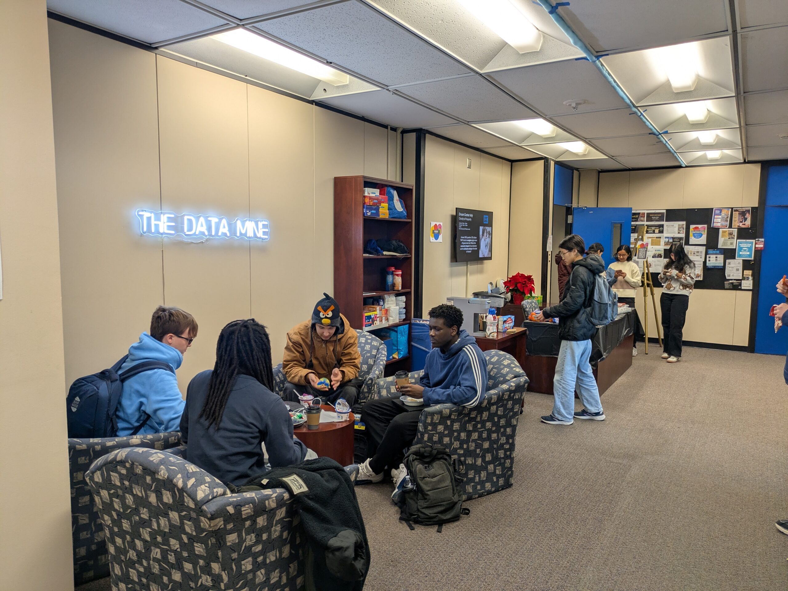 A cozy-looking space featuring students, comfortable chairs, and a neon sign that says "The Data Mine".