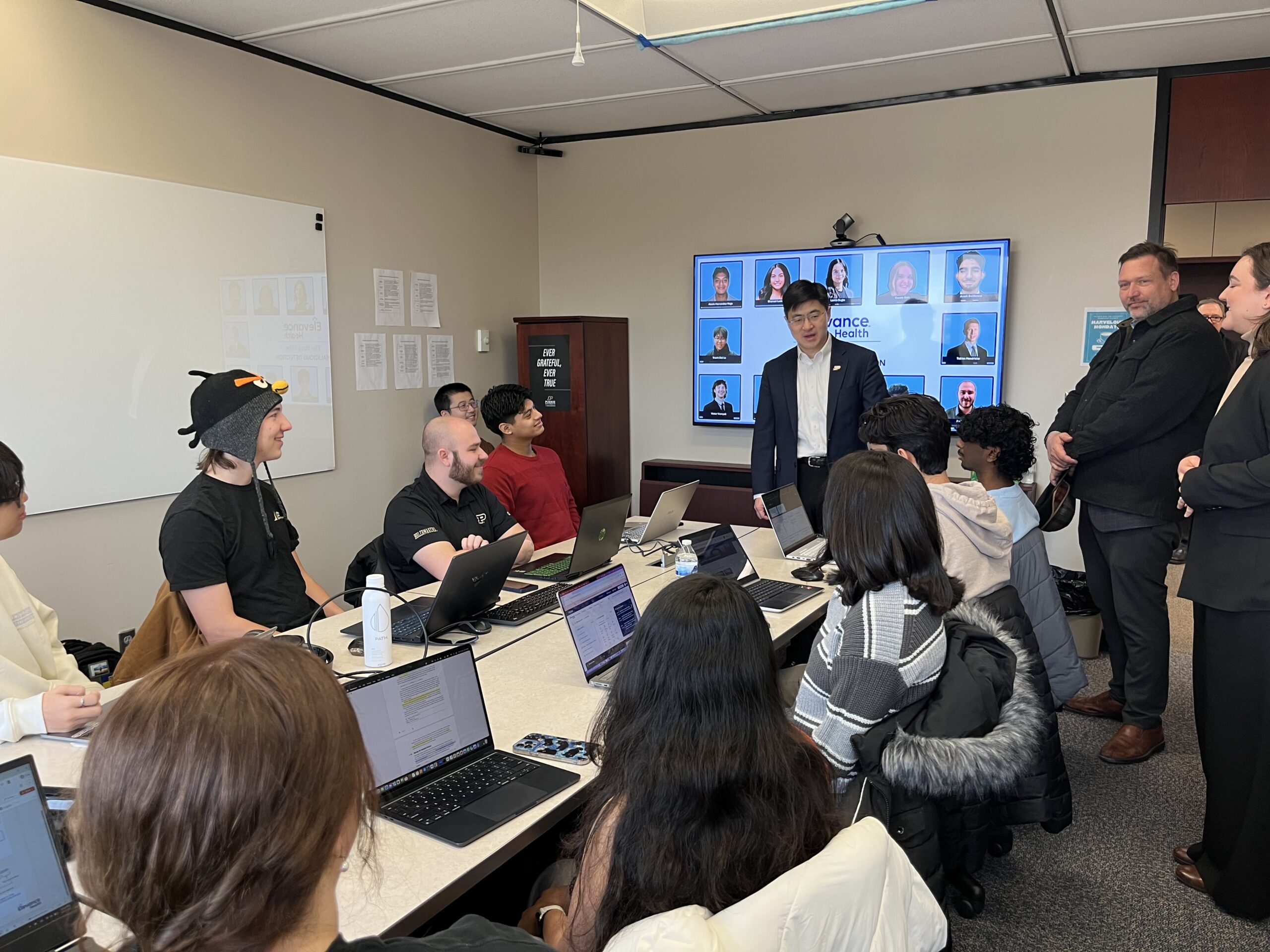 Students sit around a conference table, looking at a TV.